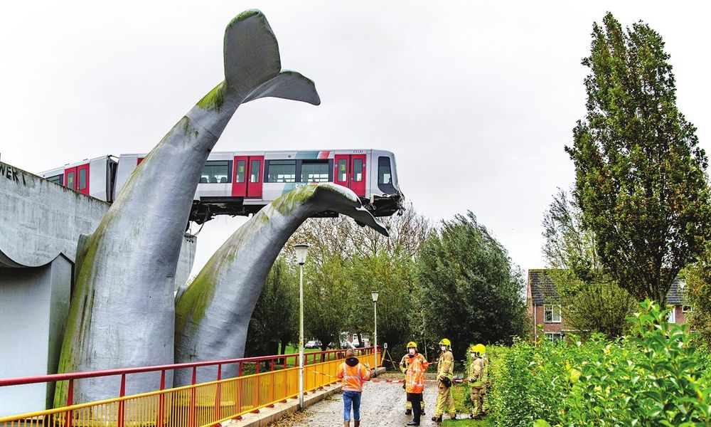 Photo of a train teetering over the track, supported by a sculpture of a whale tail